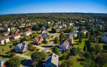 Shot using a drone during the golden hour shows an upscale suburbs with gold course, lake, houses and roof tops