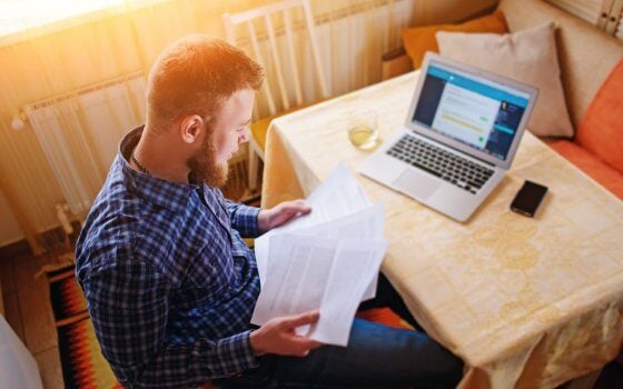 Businessman at home, he is working with a laptop, checking paperwork and bills.