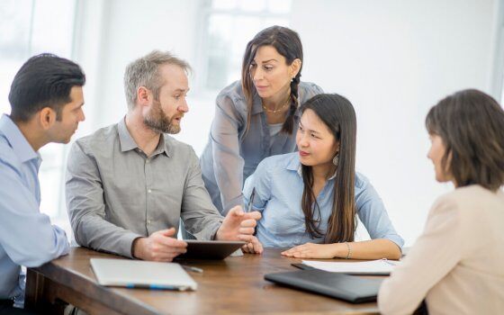 A multi-ethnic group of business professionals are looking at the companies customer reports and reviews on a digital tablet.