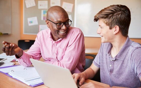 High School Tutor Giving Male Student One To One Tuition At Desk