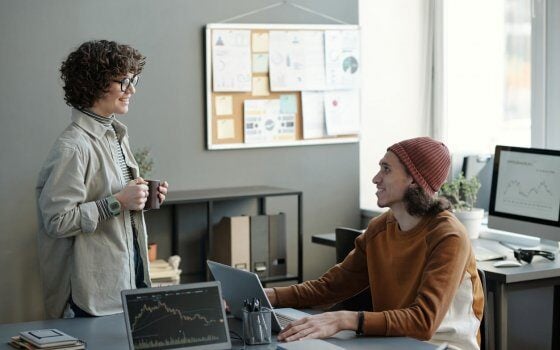 Happy young male analyst or broker looking at female colleague with cup of coffee and listening to her during discussion of stock market