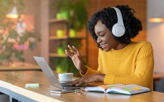 Afro girl in headset using laptop at cafe, having skype conference, free space