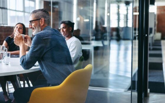 Cheerful mature businessman attending a meeting with his colleagues in an office. Experienced businessman smiling while sitting with his team in a meeting room. Creative businesspeople working together.