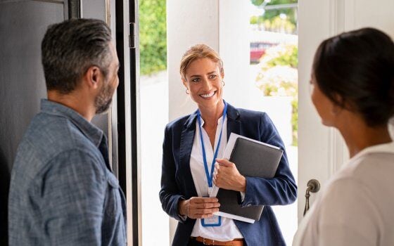 Smiling mature social counselor meeting mature couple at home. Happy multiethnic man and latin woman greeting agent at home standing near door. Successful social worker consultant on the doorstep meeting ethnic couple.