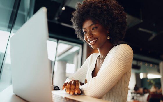 Smiling young african woman sitting with laptop in cafe, portrait