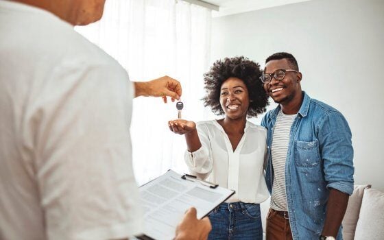 Handsome Real Estate Agent is giving key to the new apartment to happy young couple. Couple buying new apartment.  A young couple receive the keys to their new apartment from a letting agent.