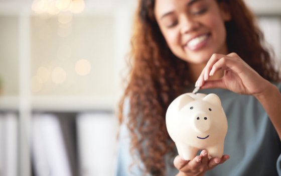 One happy young mixed race woman holding a piggybank and depositing a coin as savings. Hispanic woman budgeting her finances and investing money into her future. Saving funds for financial freedom