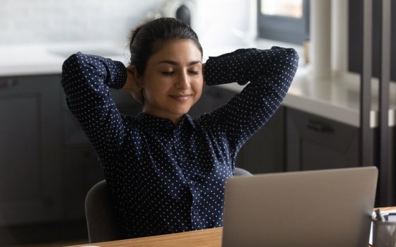 Calm young Indian woman sit at desk distracted form computer work sleep or doze off at workplace. Happy ethnic female relax at table in home office, relieve negative emotions. Stress free concept.