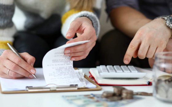 Close-up view of man and woman making account of family income. Writing down and calculating expenses. Attentive review of finance. Calculator on desk. Economy concept