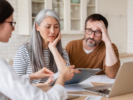 Financial advisor lawyer consulting mature middle-aged couple showing them debts, bunkruptcy, negative test results, mortgage, divorce certificate contract pension at home indoors