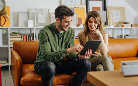 Smiling business man and business woman sitting on a orange sofa and working together on a digital tablet