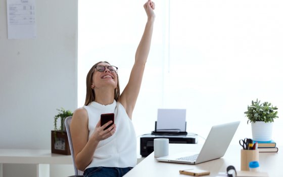 Portrait of business young woman celebrating a victory while working with mobile phone in the office.