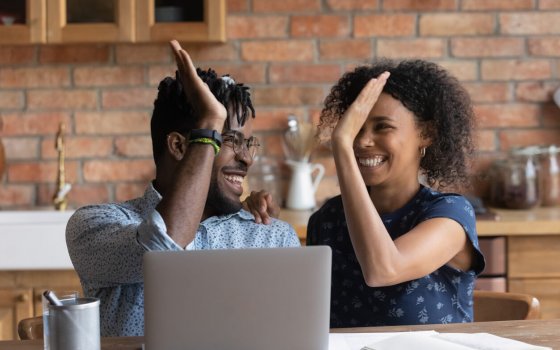 Happy excited Black mixed race couple celebrating financial success at laptop, getting income, loan, mortgage bank approval, planning good family budget. Young husband and wife giving high five