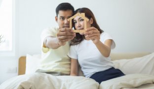 Couple or 2 asian people on bed in bedroom, home or house. Man and woman hold home model in hand together. Look happy, romantic. Concept for married, family, rent, buy, real estate and propertry.